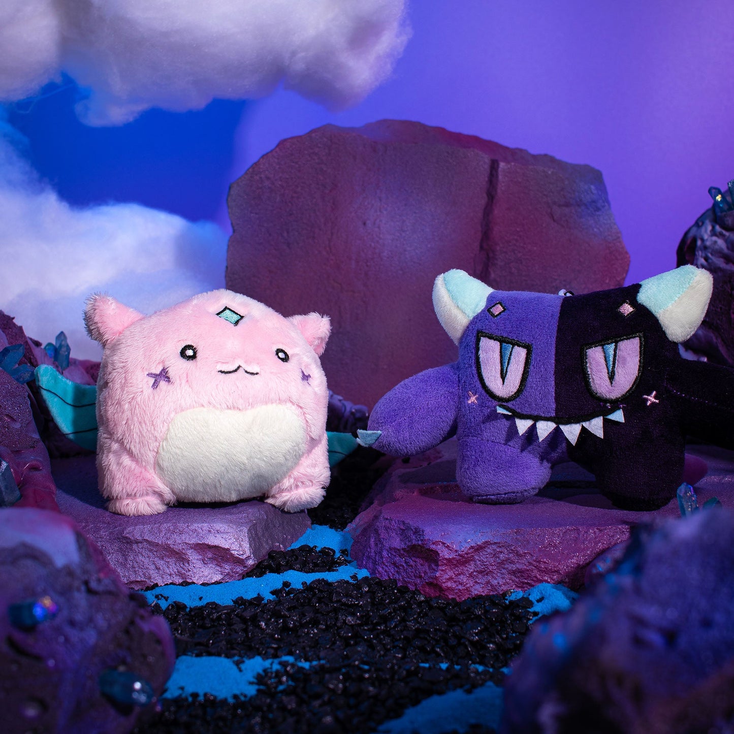 Gleam and Gloom plush keychains posed together on a purple rocky set under a painted sky.