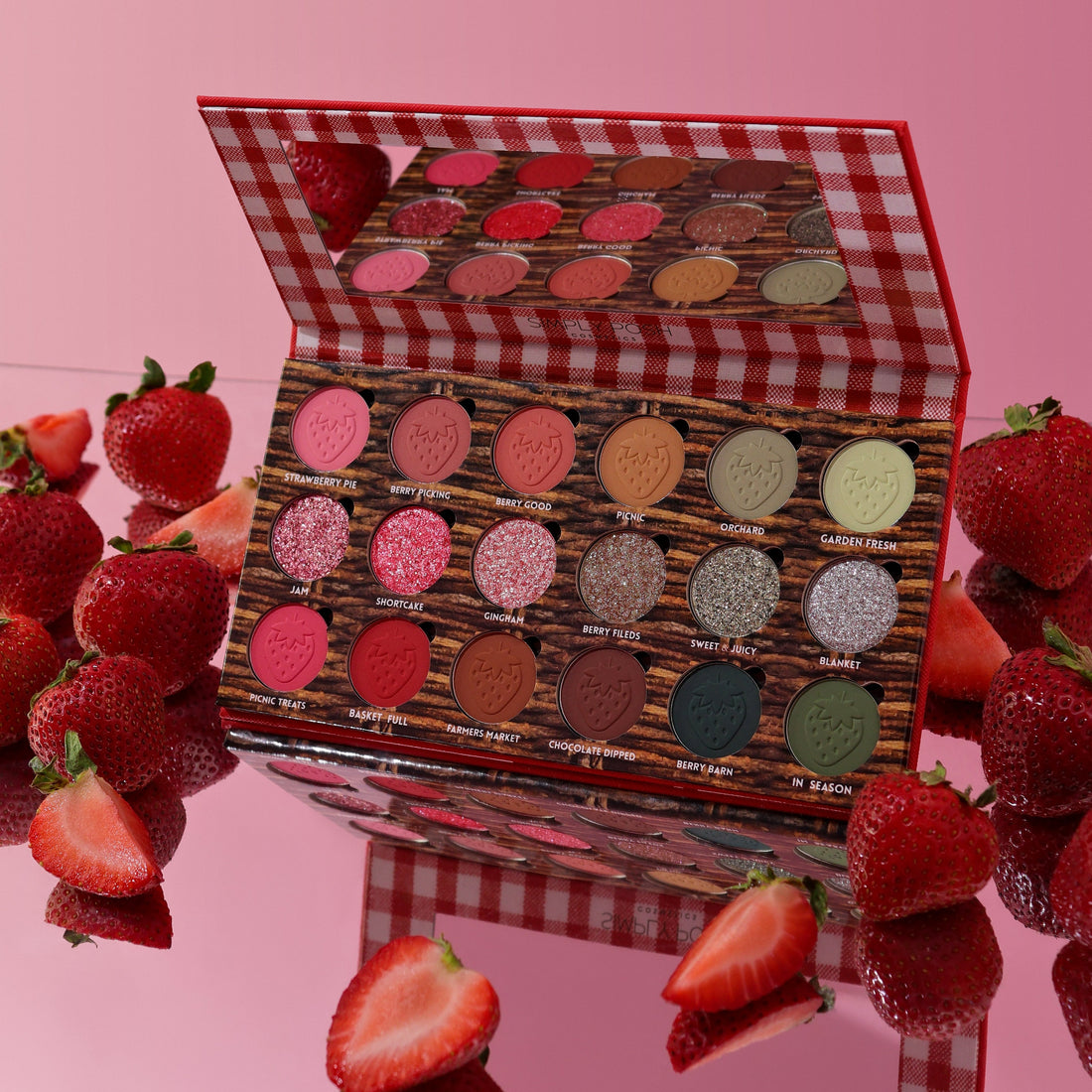 Strawberry Picnic palette open on a pink surface surrounded by fresh strawberries, mirror lid reflecting the pans