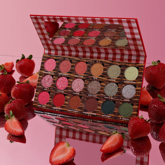 Strawberry Picnic palette open on a pink surface surrounded by fresh strawberries, mirror lid reflecting the pans