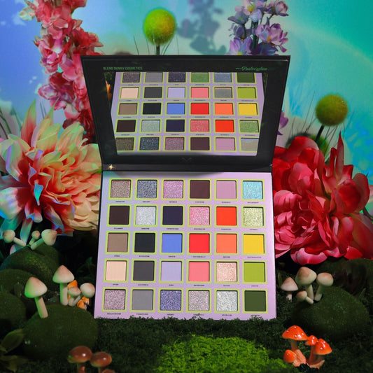 Psilocybin eyeshadow palette open, 30 earthy and psychedelic shades with silvery sparkles, cover art of three nymphs in mushroom-cap headpieces