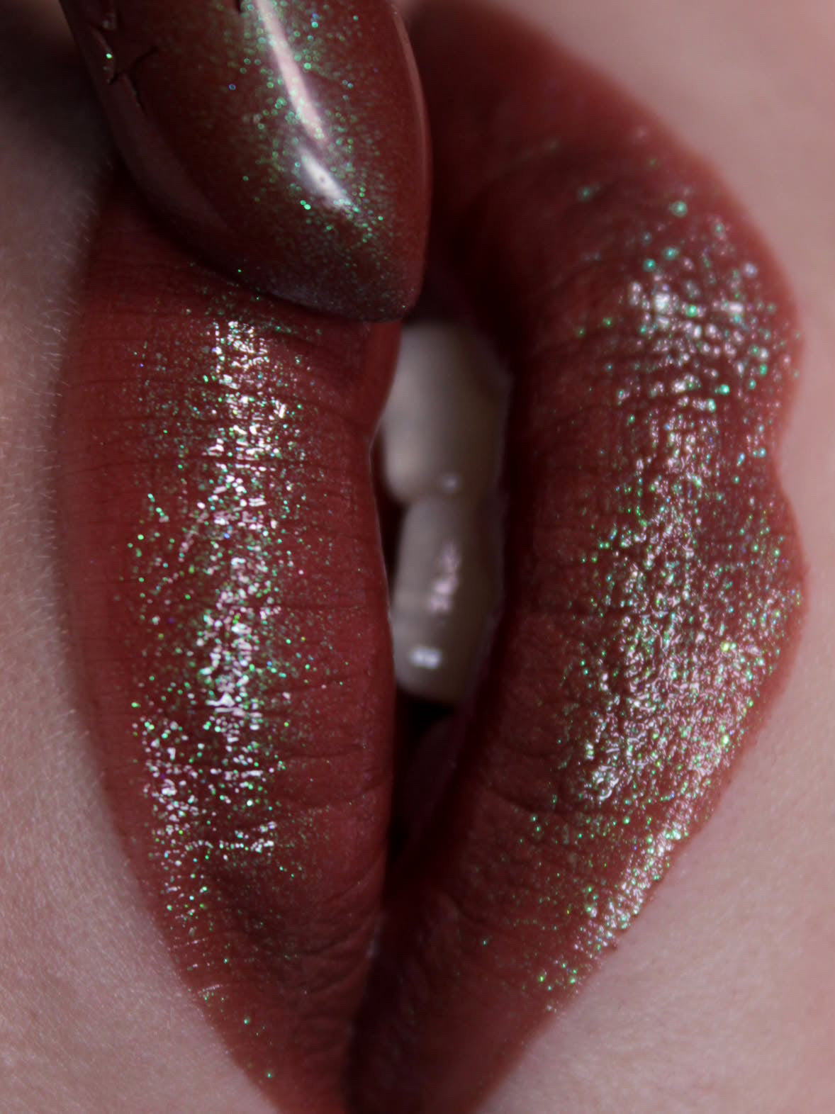 Lip close-up: deep red-brown with green and blue sparkle, bullet held to the lip.