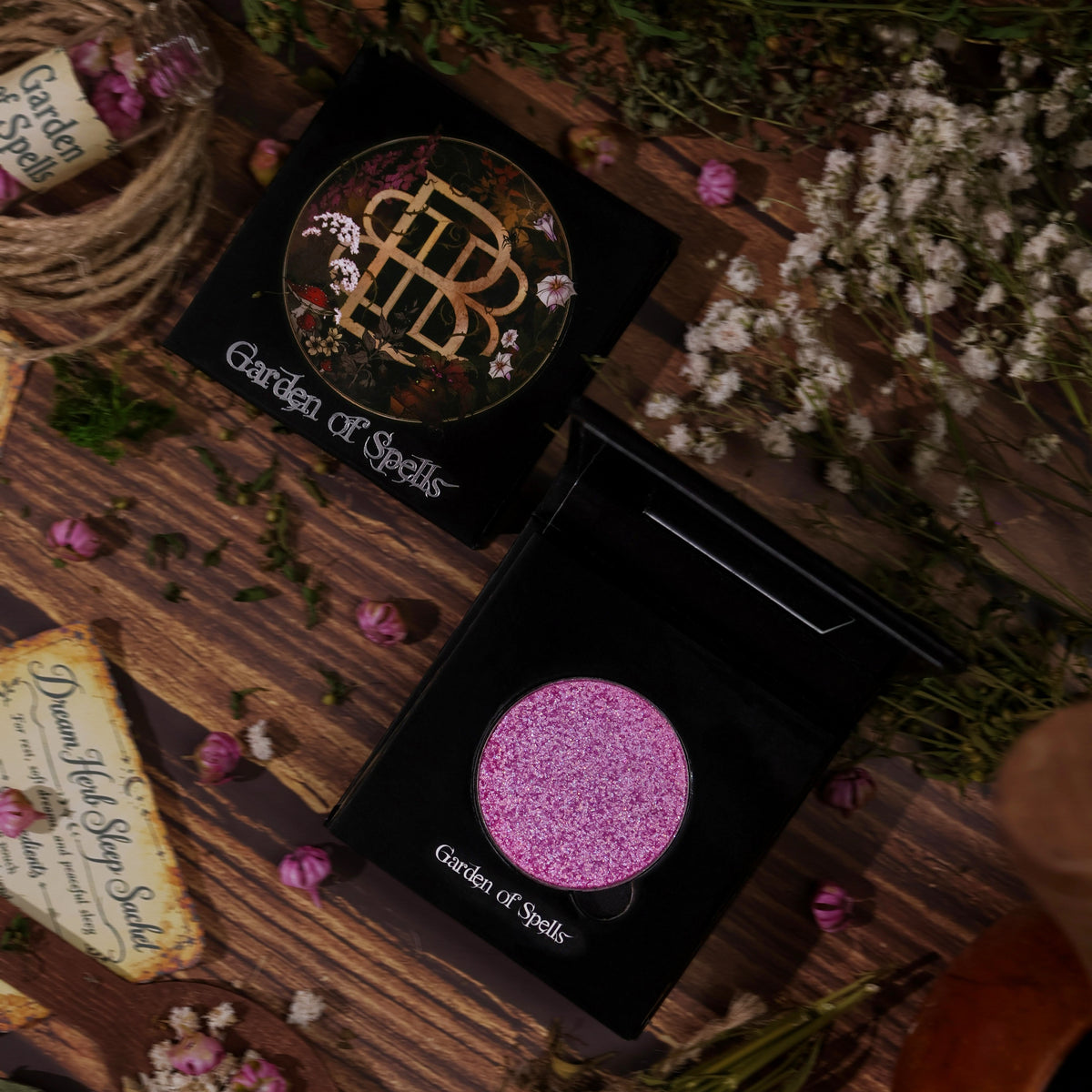 Closed compact with the gold monogram lid beside the open highlighter, on wooden boards with dried flowers.