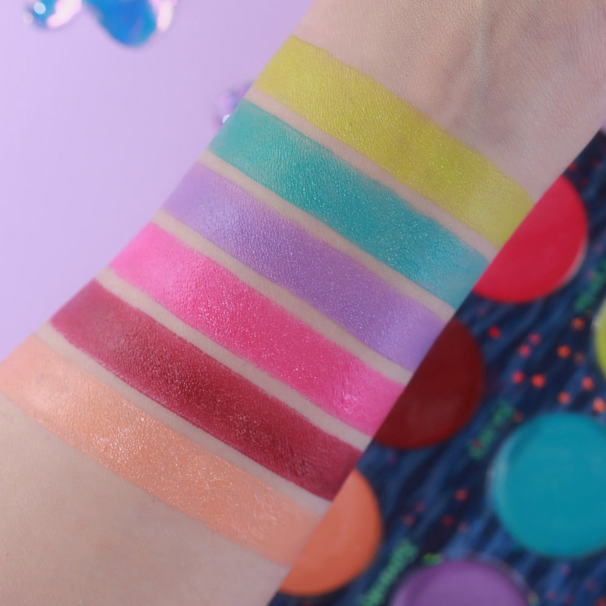 Unlabelled arm swatches on light skin beside the open palette, on a lilac background.