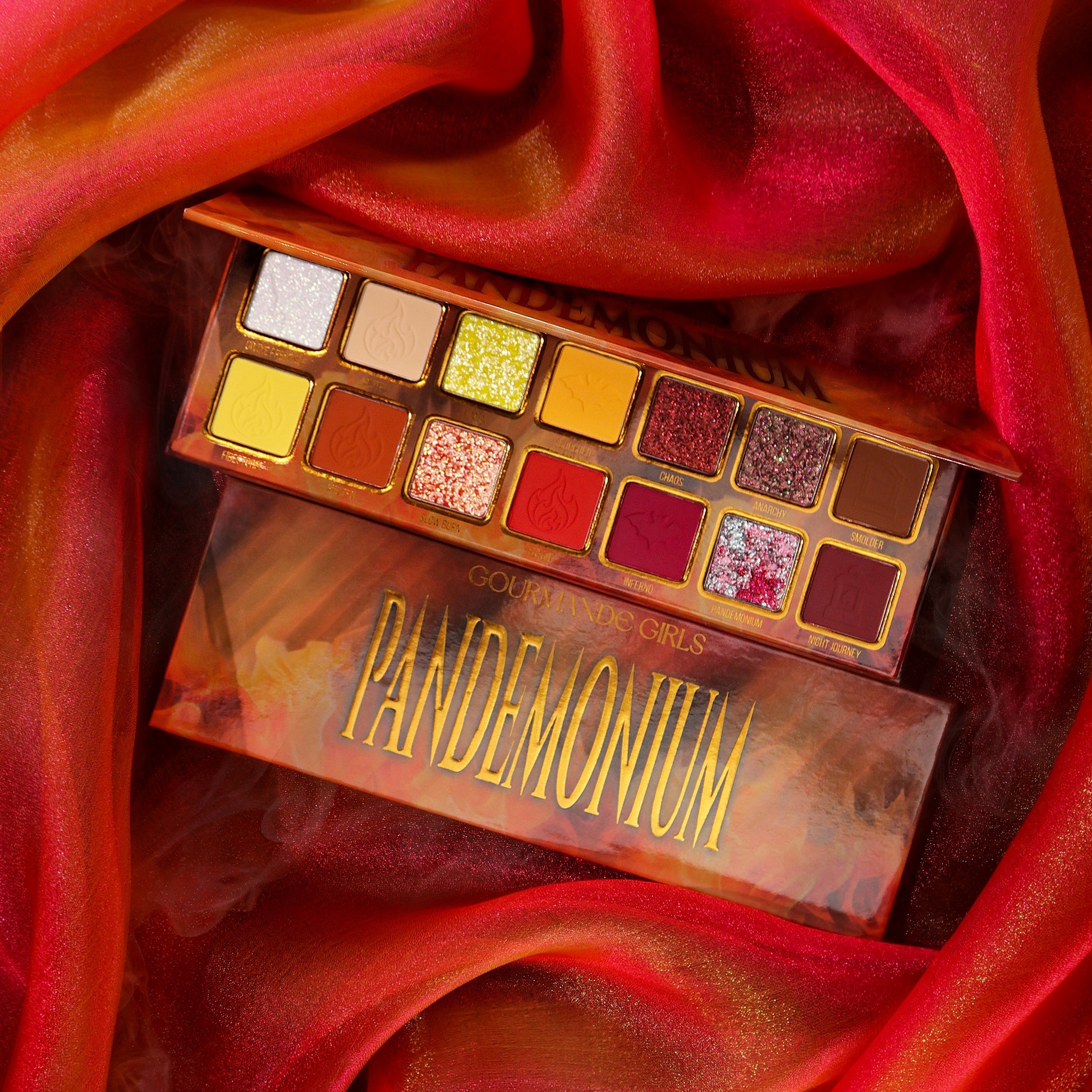 Gourmande Girls Pandemonium eyeshadow palette open on red silk, 14 shades in two rows of gold-framed pans, from pale sparkles to yellows, rusts, reds and plum