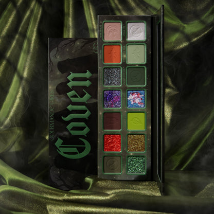 Gourmande Girls Coven eyeshadow palette open beside its box on green satin, 14 pans of greens, orange, red, plum, purple and sparkling shifts