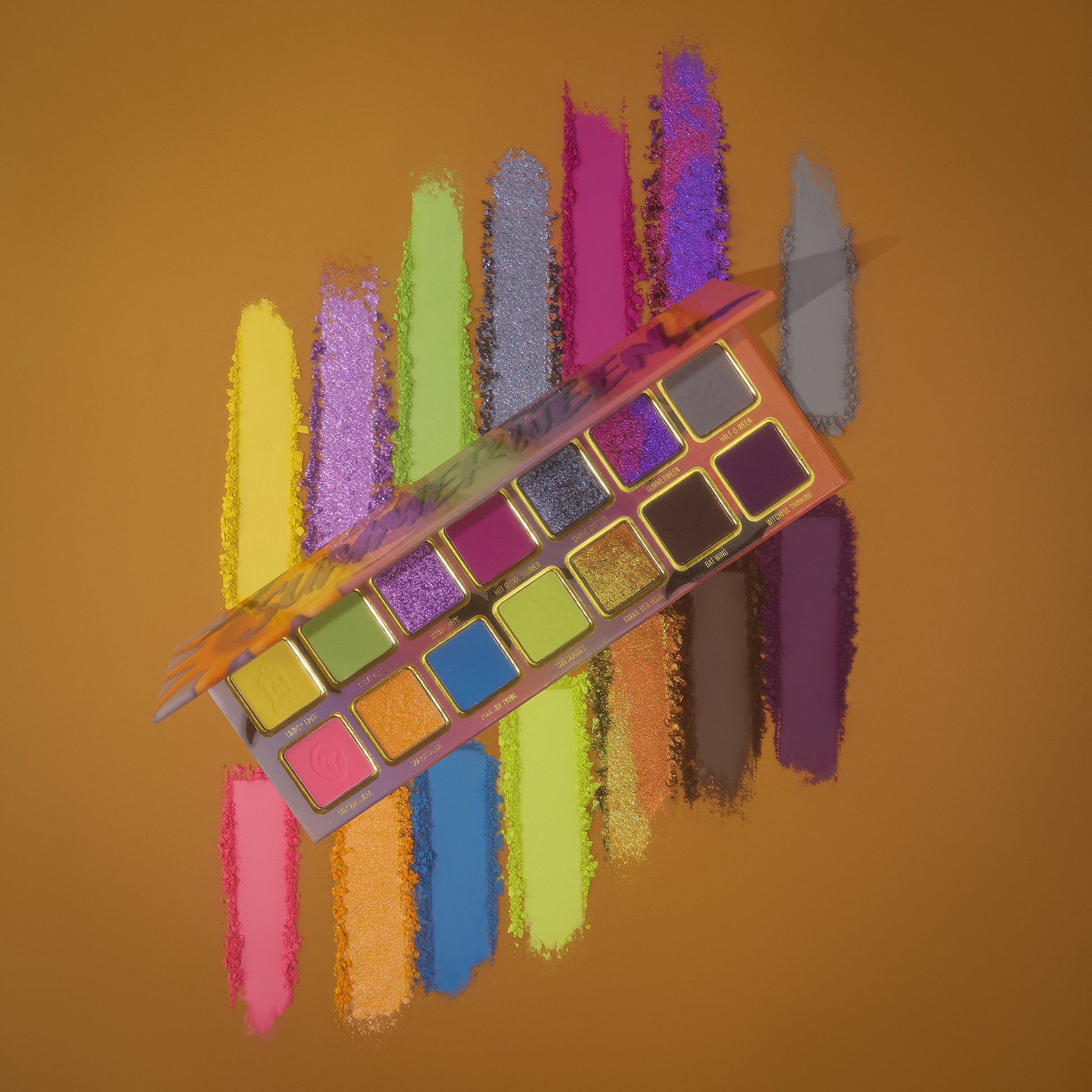 Summerween palette tilted over powder swatch streaks of yellow, purple, green, blue, pink, and copper on a mustard background