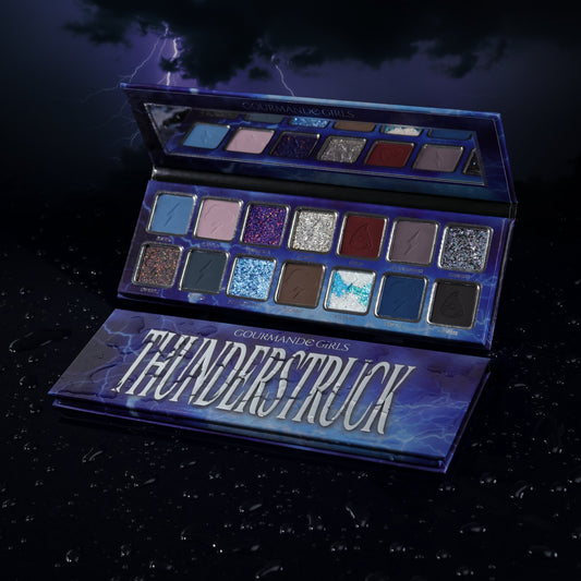 Gourmande Girls Thunderstruck eyeshadow palette open against a lightning sky, 14 shades in two rows of silver-framed pans, blues, greys, purples and sparkles