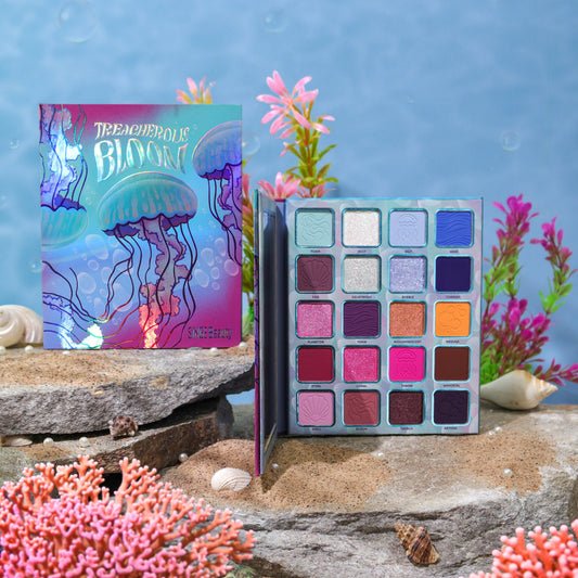 Treacherous Bloom palette open beside its jellyfish box on stones and sand, with pink coral, seashells, and pearls