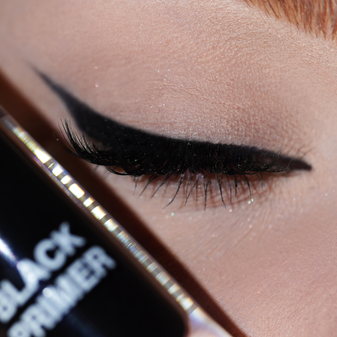 Closed eye with bold black winged liner drawn using the primer, with the Black Primer bottle resting against the cheek.