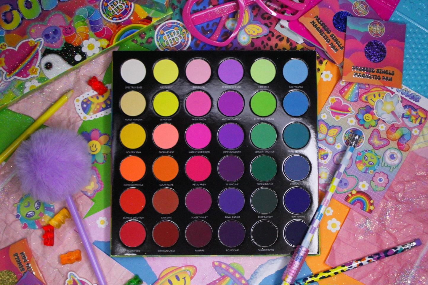 Arch of Color palette open and flat among kawaii stickers, heart sunglasses, and pom pencils, 36 matte pans seen top-down