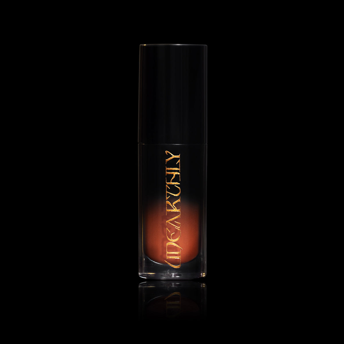 October in a clear tube with a black cap and gold Unearthly logo, the rusty orange cream showing through