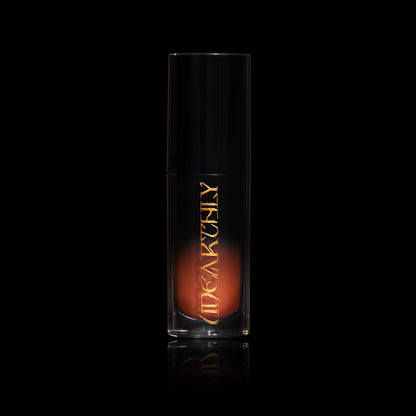 October in a clear tube with a black cap and gold Unearthly logo, the rusty orange cream showing through