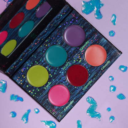 Two Creepy Creams palettes overlapping on a lilac surface with blue jelly droplets, the six cream pans labelled Eerie through Ghastly.
