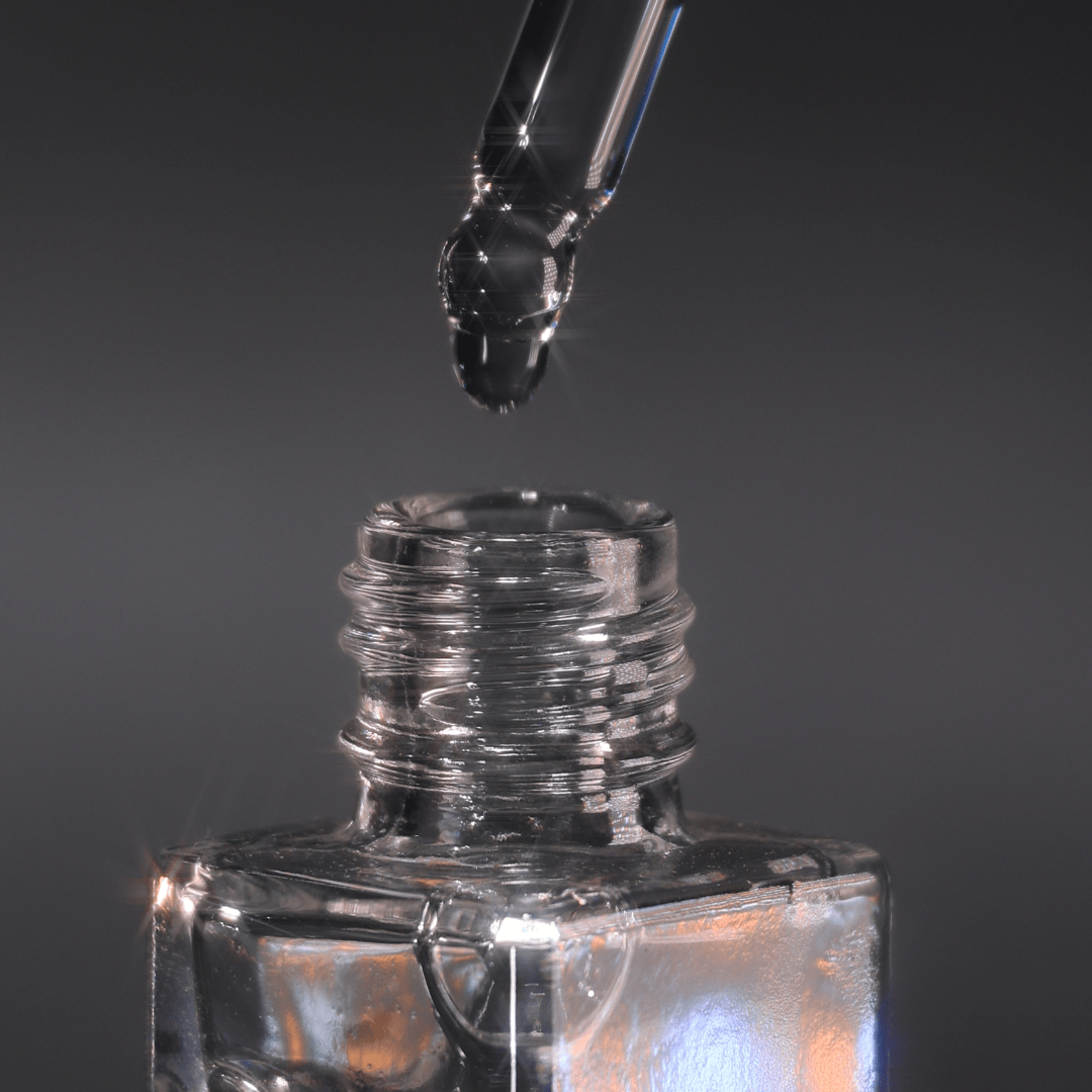 Glass dropper lowering a clear drop into the open neck of the Mixing Medium bottle on a grey background.