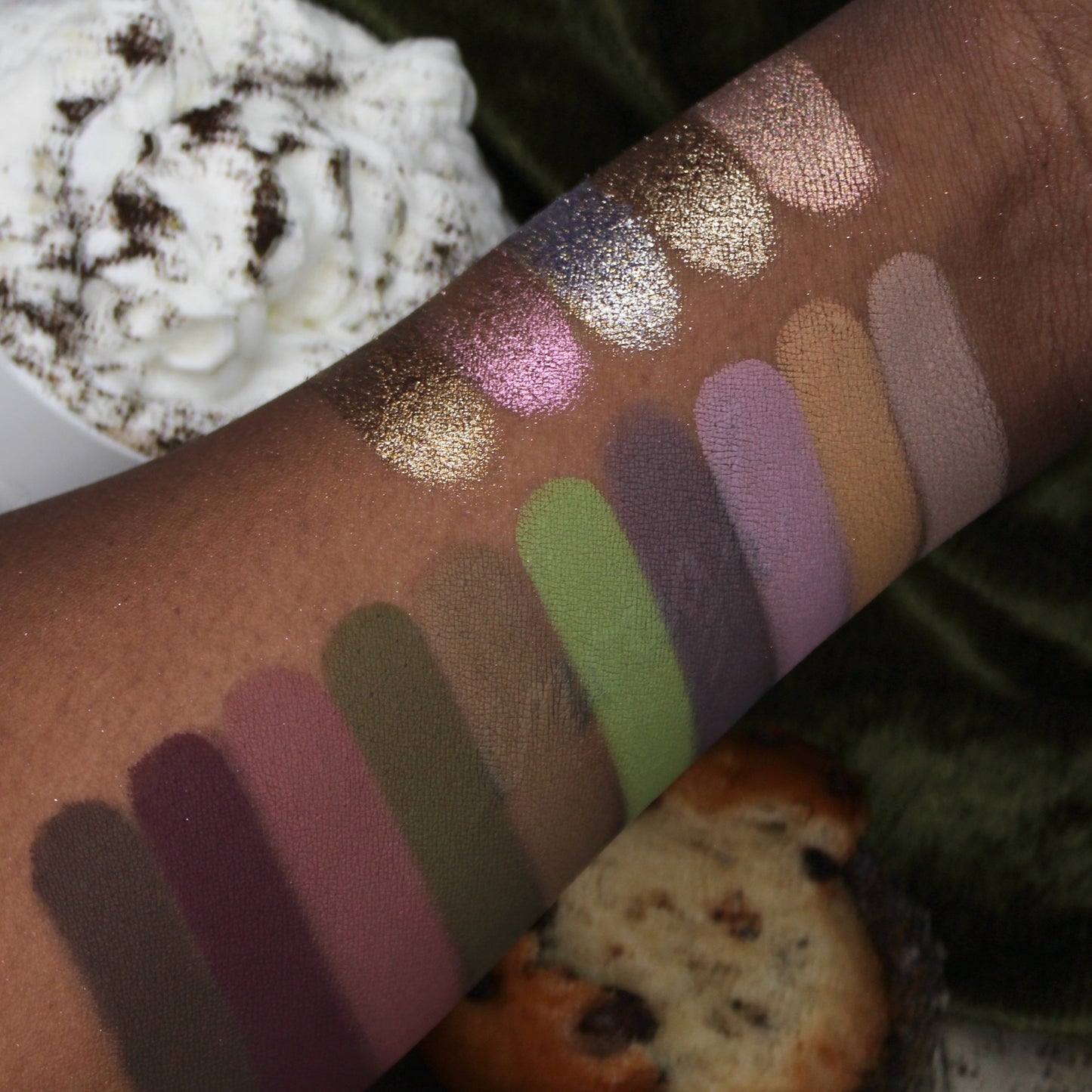 Color swatches on a person's arm with a blurred background of a dessert and cookie.