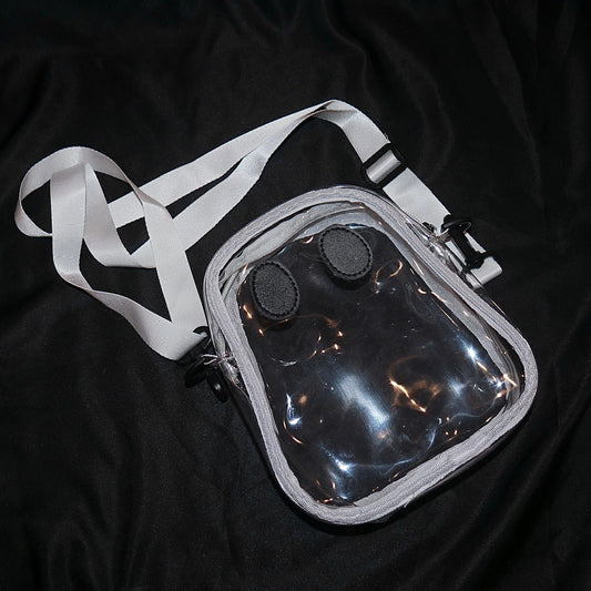 The clear Ghostie bag laid flat with its adjustable strap unclipped, showing the ghost shape and the two sewn-on eyes