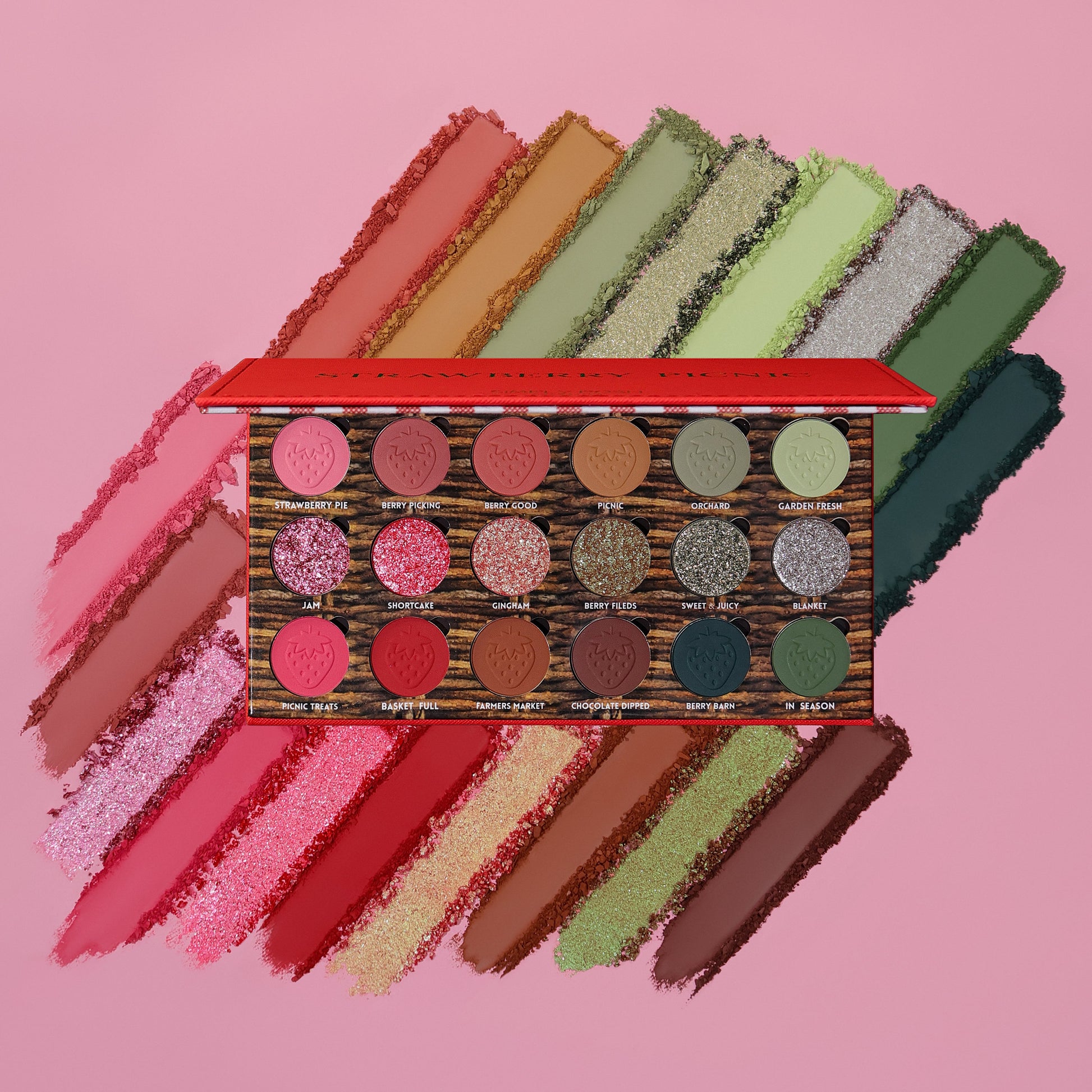 Strawberry Picnic palette open over swatch smears on pink, 18 pans in three rows of reds, browns, and greens with six shimmer pans