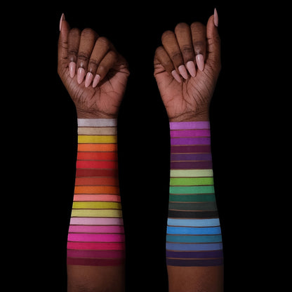 All 36 shades swatched down two forearms on two deep skin tones, full rainbow range from warm reds to cool blues and purples