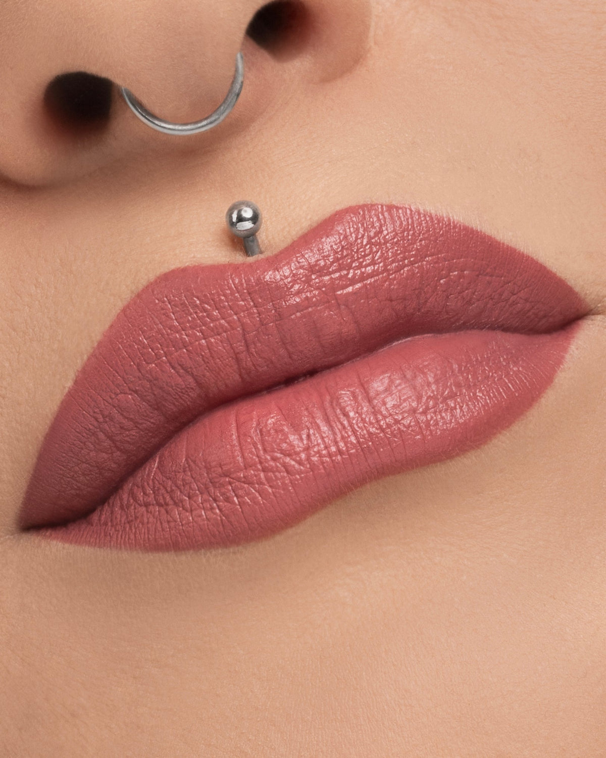Unearthly Cosmetics Bewitched Menacing Cream lipstick worn on the lips, mauvy pink on a fair skin tone with a septum ring and lip piercing in frame