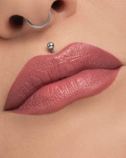 Unearthly Cosmetics Bewitched Menacing Cream lipstick worn on the lips, mauvy pink on a fair skin tone with a septum ring and lip piercing in frame