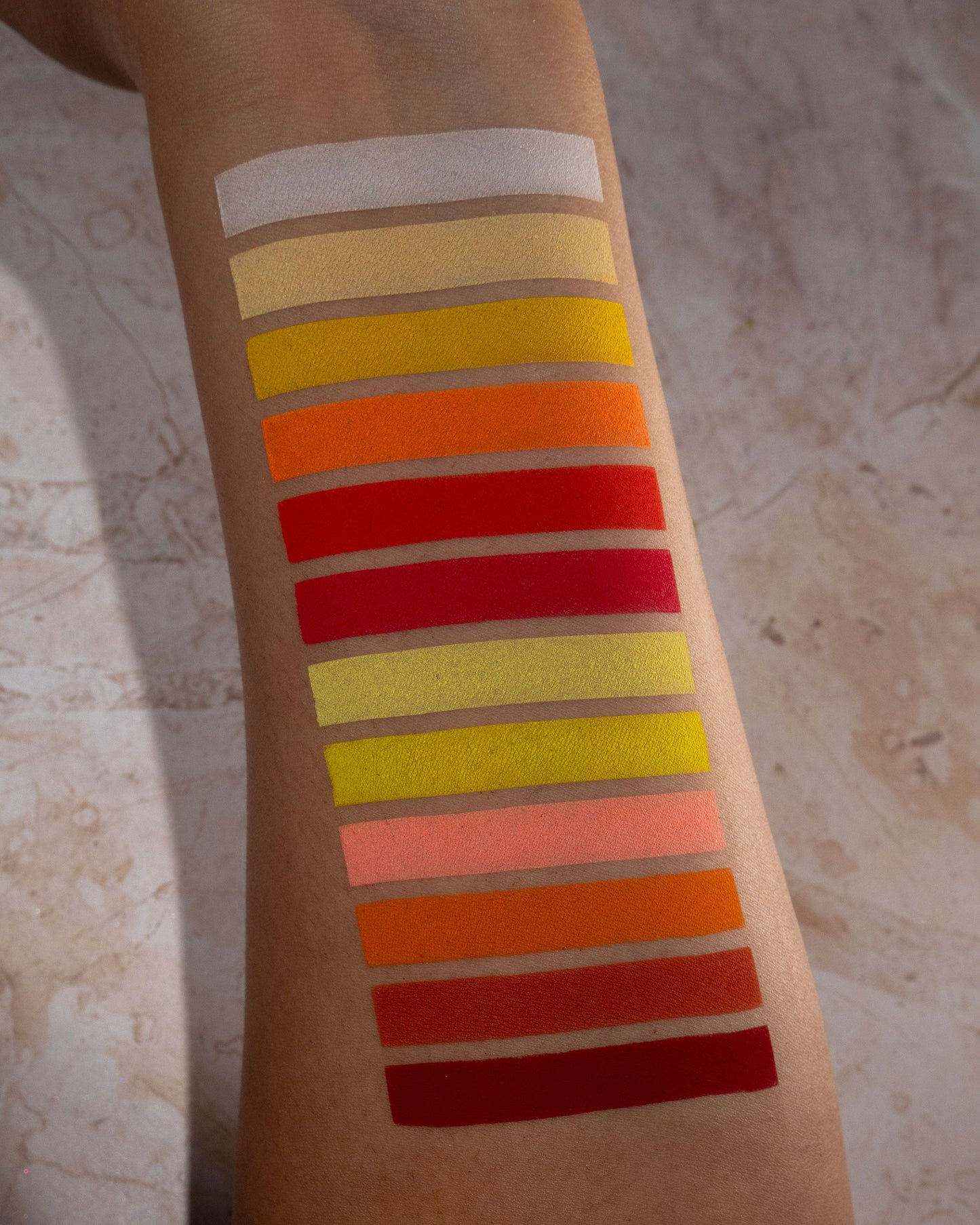 Warm shades swatched down a forearm on tan skin, from white and pale yellow through gold, orange, and true red