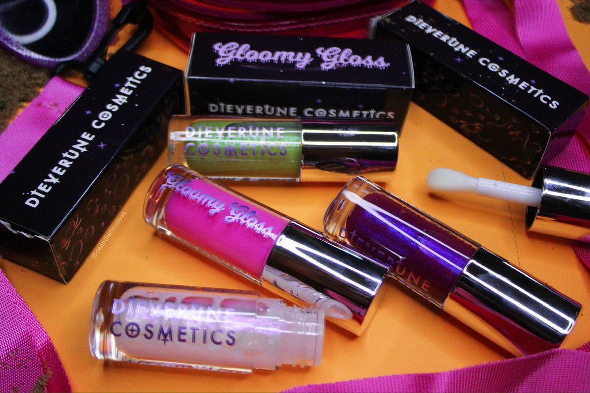 Flatlay of the Gloomy gloss tubes and their printed boxes on an orange and purple backdrop