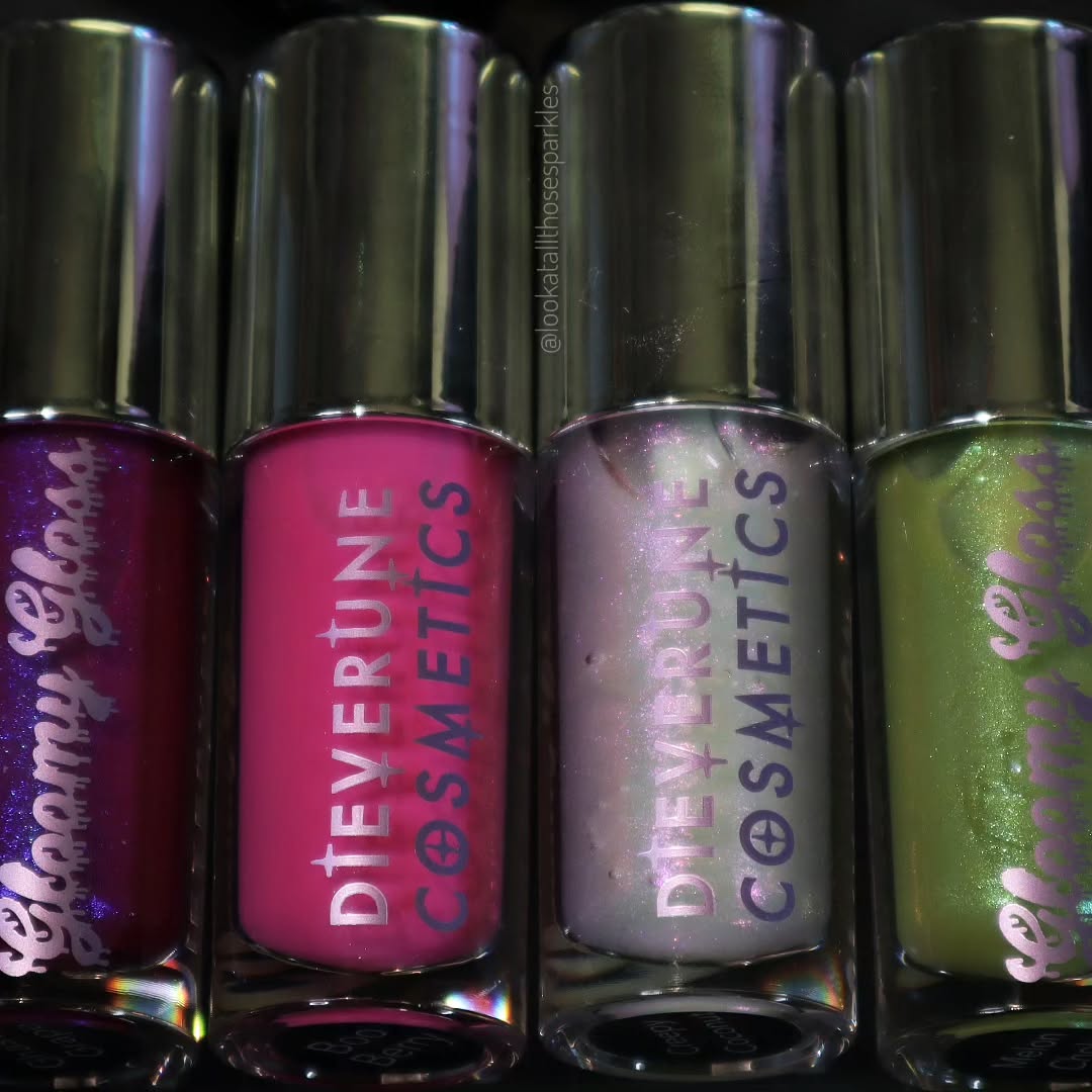 The four Gloomy gloss tubes standing upright in a row, showing the berry, pink, clear and green bases