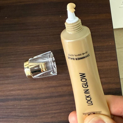 Gold shimmer base tube with the clear gold-rimmed cap removed, pale gold product on the applicator tip, dark wood surface