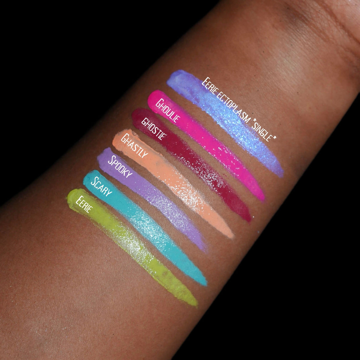 Labelled arm swatches on deep skin against black, the six cream shades plus one extra swatch of a separate single.