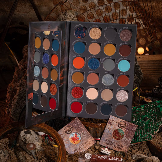 Wasteland palette open on rusted scrap, 24 named pans in rusted reds, burnt oranges, teals and sandy neutrals, with two pressed single pans in front.