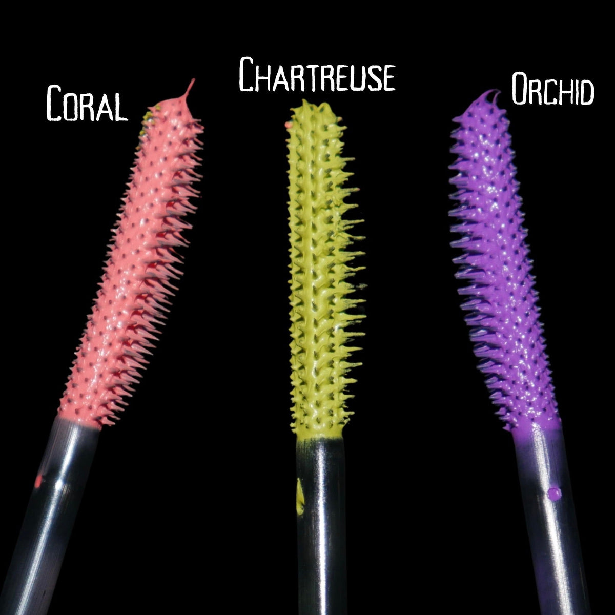 The three loaded mascara wands side by side on black, labelled Coral, Chartreuse and Orchid.