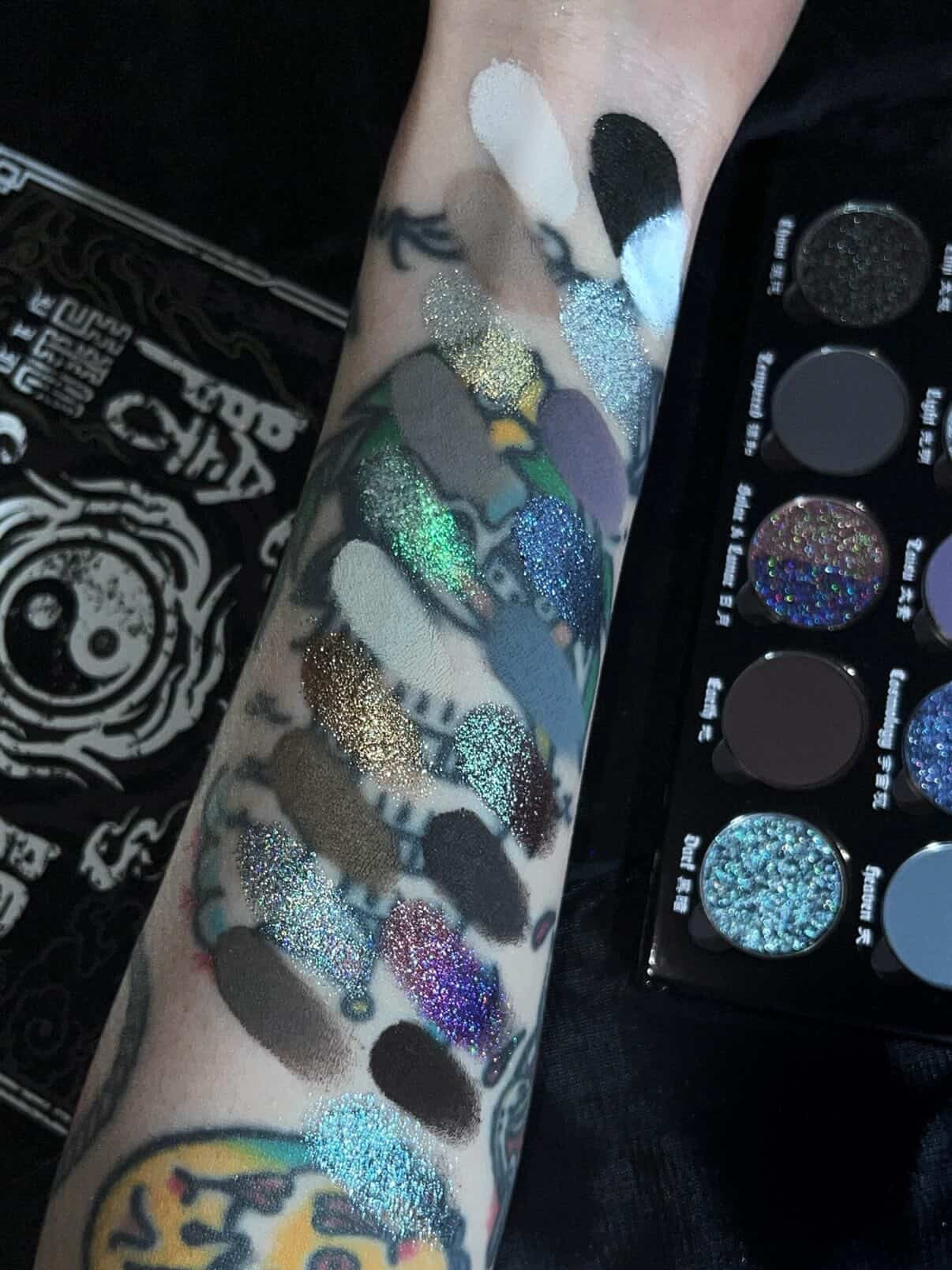 BellaBeauteBar Yin & Yang x Freya86_ff palette swatched on a tattooed arm — holographic glitters, duochromes, and deep mattes alongside the open palette