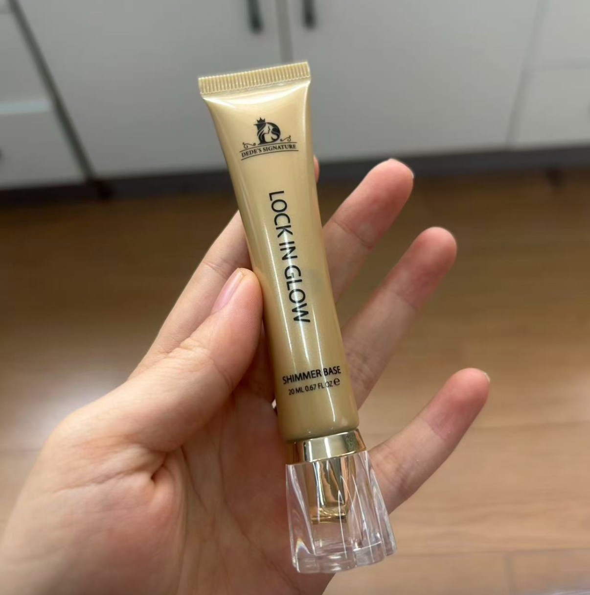 Gold Lock in Glow shimmer base tube held in hand, clear faceted cap on, kitchen background