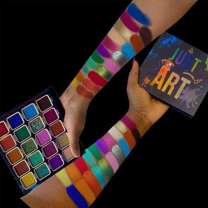 Open Just Art palette held in hand next to arm swatches on two skin tones and the box, black background