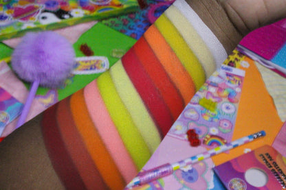 Close-up of warm orange, yellow, and red stripe swatches on tan skin over a colourful 90s sticker collage