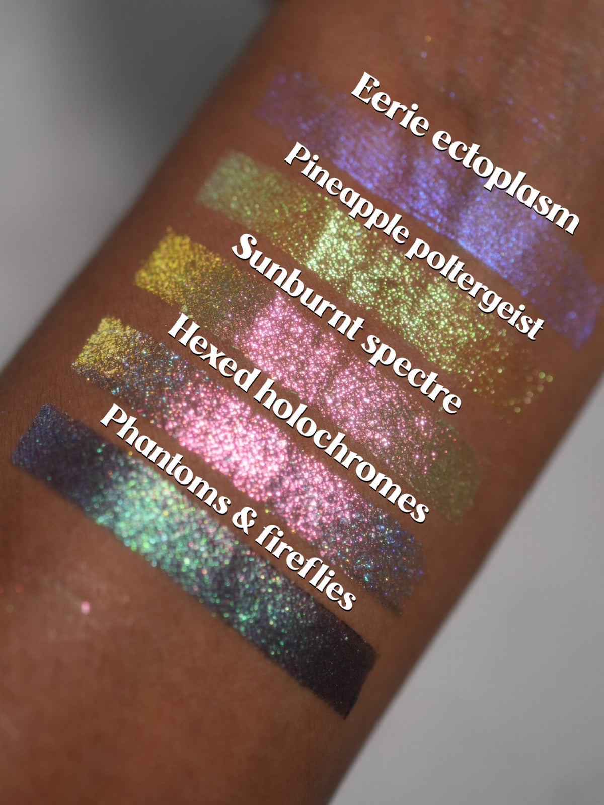 The four Summerween singles swatched on deep skin beside Eerie Ectoplasm cream highlighter, labelled