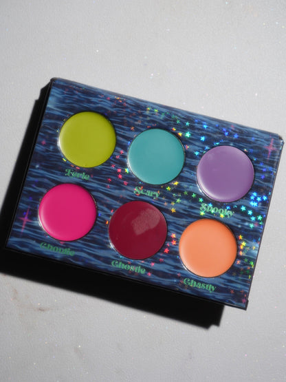 The open palette angled in daylight, six cream pans on a blue water-print tray, each labelled with its shade name.