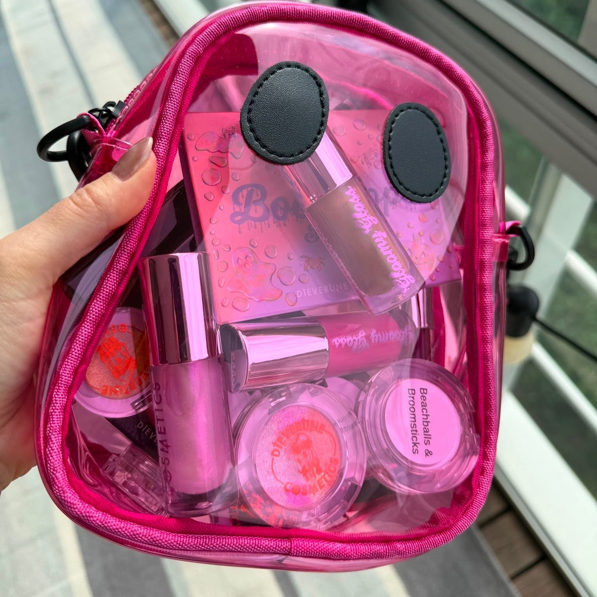 The pink Ghostie bag held in one hand, packed with compacts and glosses for scale