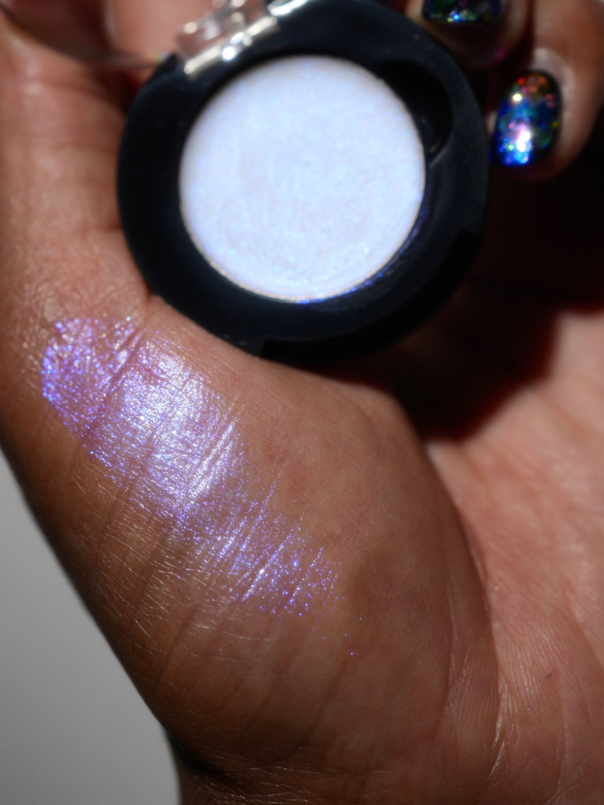 Eerie Ectoplasm compact in hand with a finger swatch on deep skin