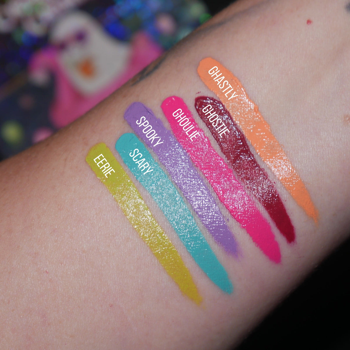Six labelled diagonal arm swatches on light skin, Eerie, Scary, Spooky, Ghoulie, Ghostie and Ghastly, with a ghost print behind.