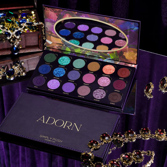 Simply Posh Adorn eyeshadow palette open beside its purple faux-leather cover with gold lettering, 18 pans of greens, blues, gold, pinks, purples, and browns