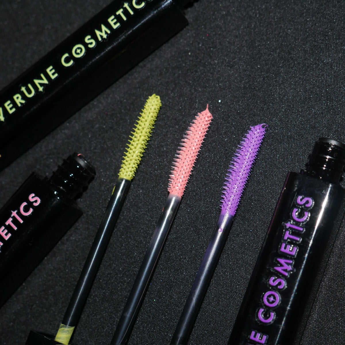 Three loaded wands laid between two tubes on black fabric, chartreuse, coral and orchid.