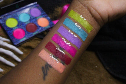 Six labelled arm swatches on deep skin beside the open palette and a skeleton hand prop, Eerie at the top to Ghastly at the bottom.