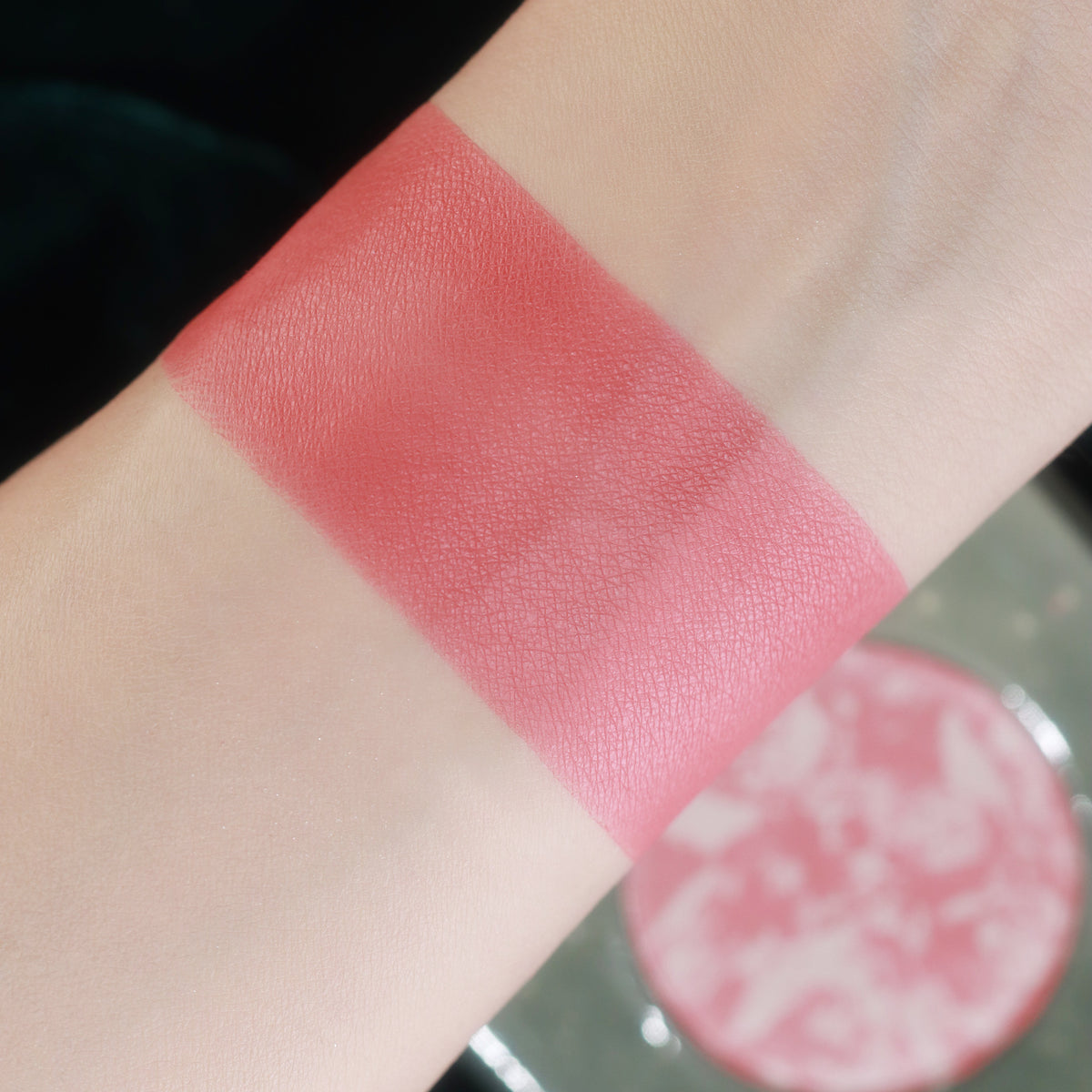 Invocation swatched on light skin beside its marbled pan, a bright rose pink