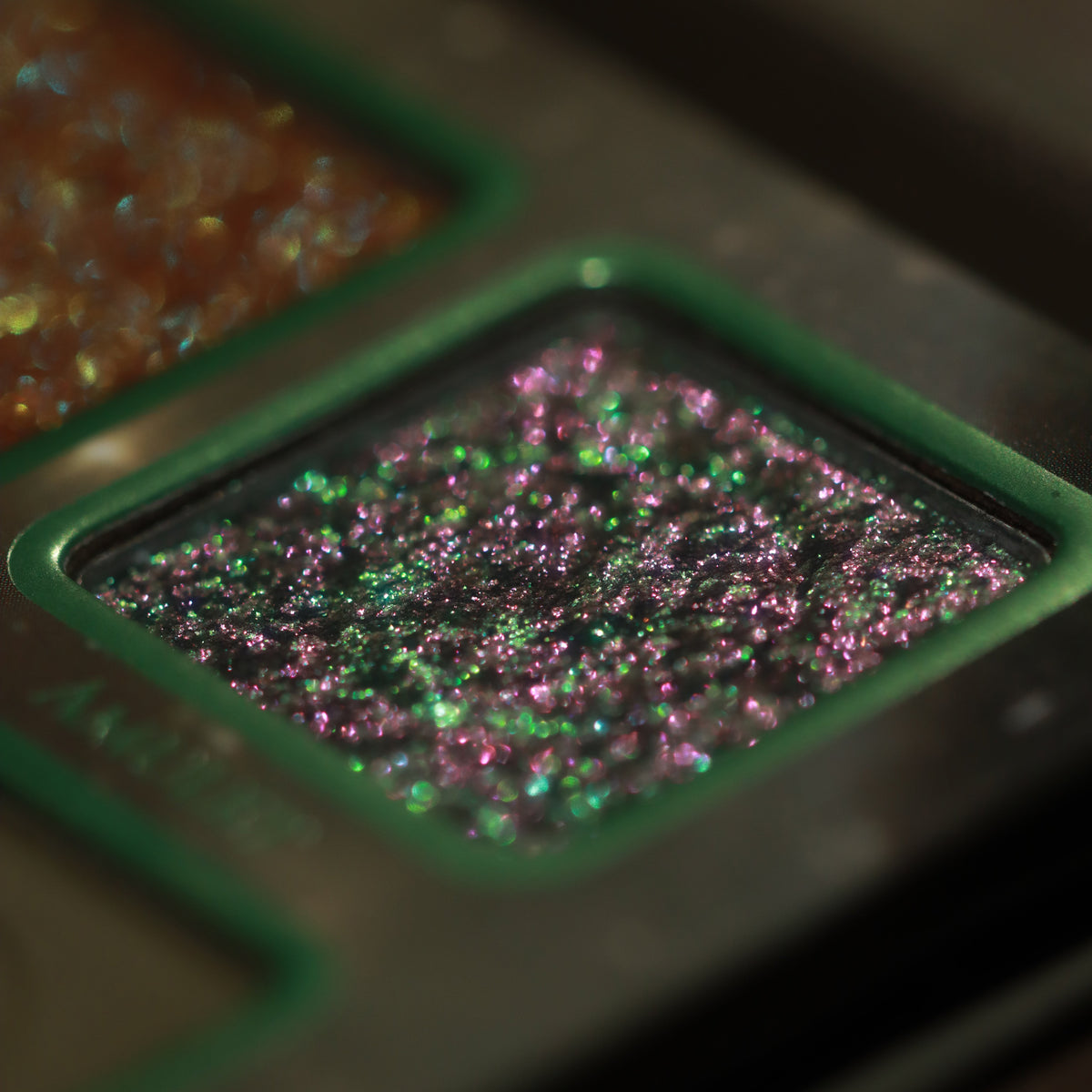 Macro of Amulet, a dark base packed with green and pink shifting sparkles