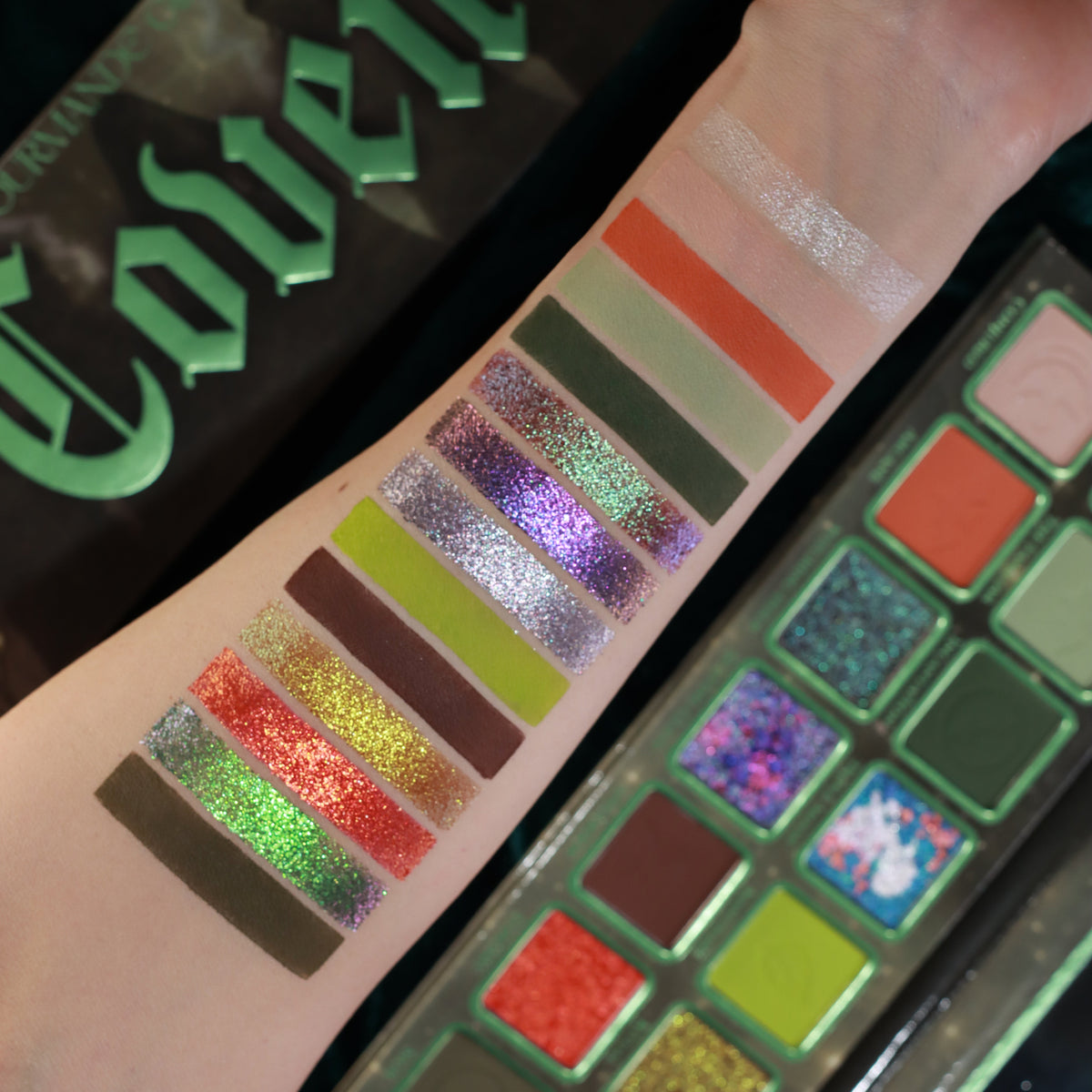 Coven shades swatched on a light-skinned arm next to the open palette and the box with its green gothic lettering