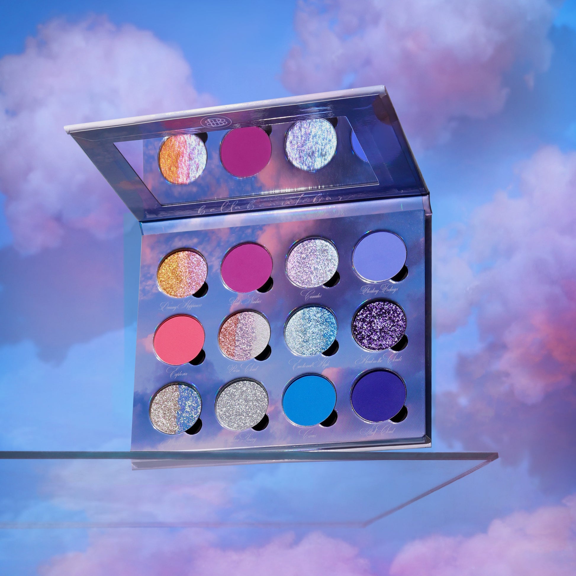 Bellabeautebar On Cloud 9 eyeshadow palette open in a cloud scene, showing 12 pans of pastel multi-chrome shimmers and blue, purple, and coral mattes