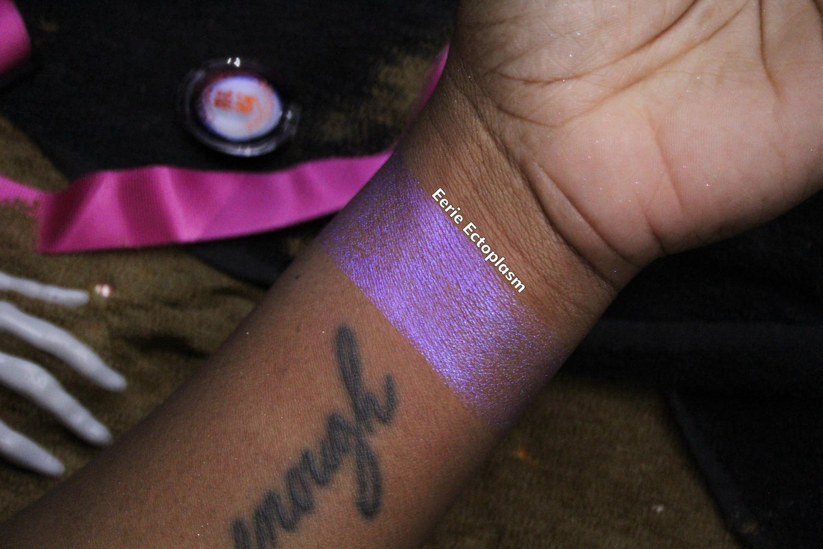 Eerie Ectoplasm arm swatch on deep skin, labelled, with the open compact behind