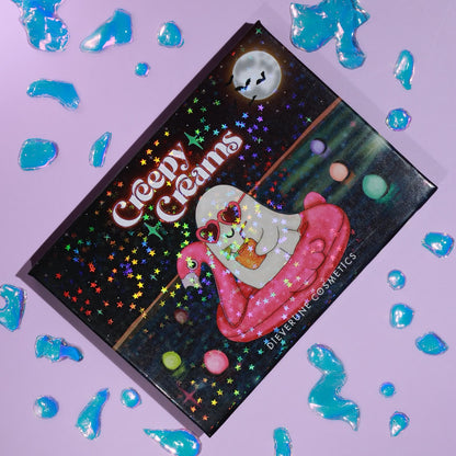 The closed palette on lilac with blue jelly droplets, its holographic lid showing a ghost in sunglasses on a pink flamingo float under a full moon.