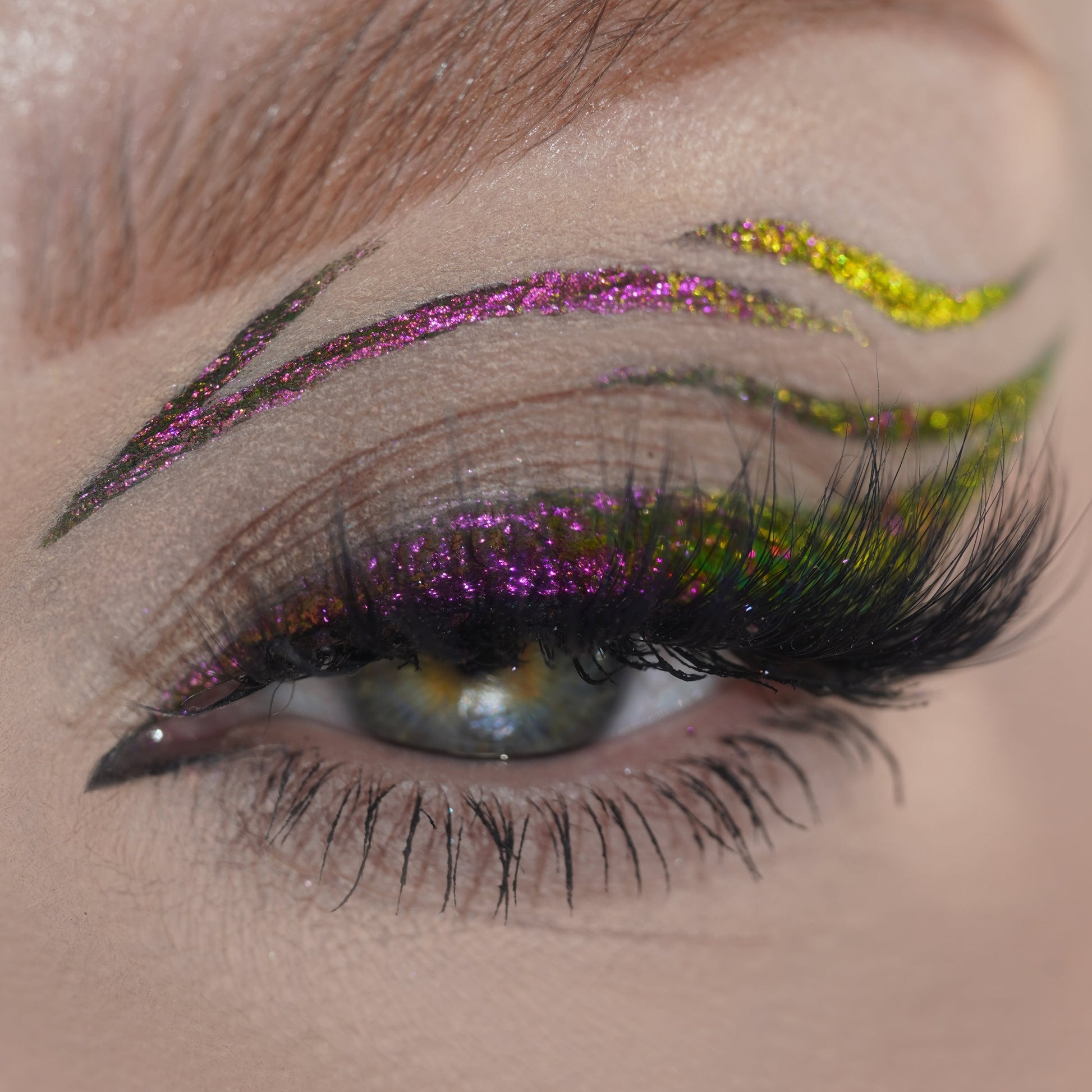Close-up of a closed eye with magenta and orange graphic liner curling over the lid, plus small painted dots above the cheekbone.